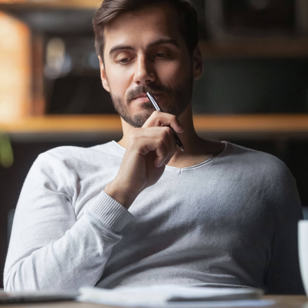 Person in a grey sweater holding a pen, managing intrusive thoughts at a desk in NYC.