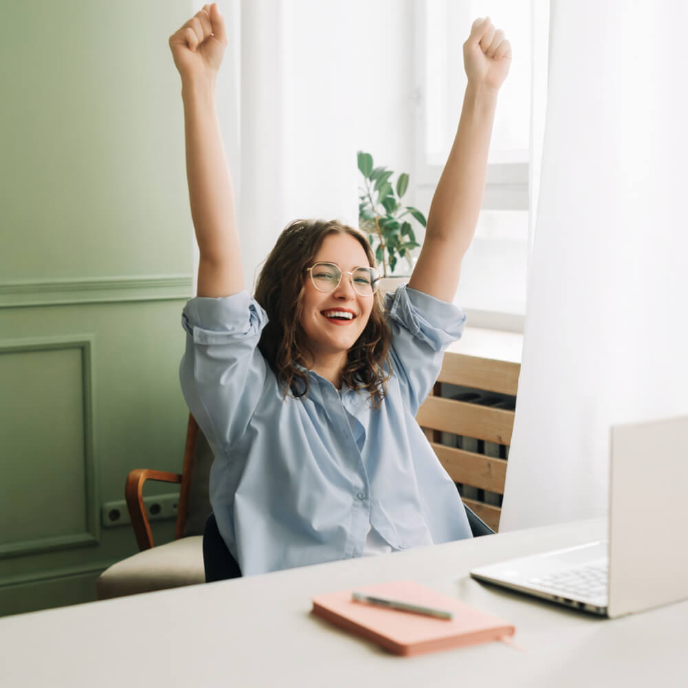 Person with raised arms at a desk with a laptop, focusing on improving employee well-being in NYC.