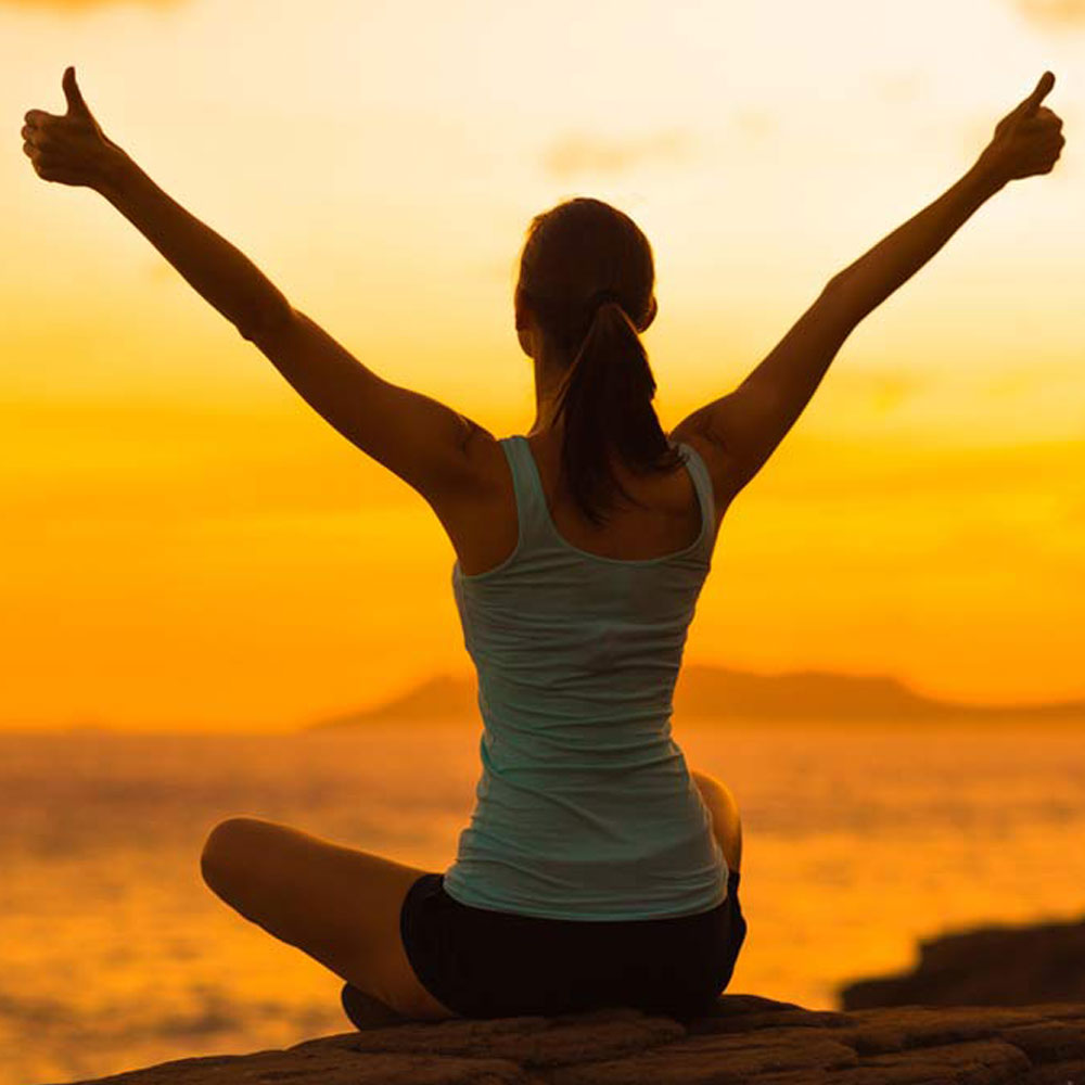 Woman with thumbs up, sunset backdrop, navigating life transitions with NYC psychotherapy.