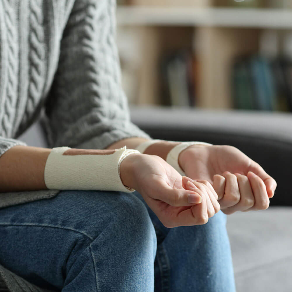 Person with wrist brace, overcoming self-harm addiction in NYC home setting.