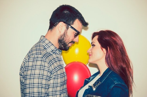 Two people holding a red balloon between them against a beige background.